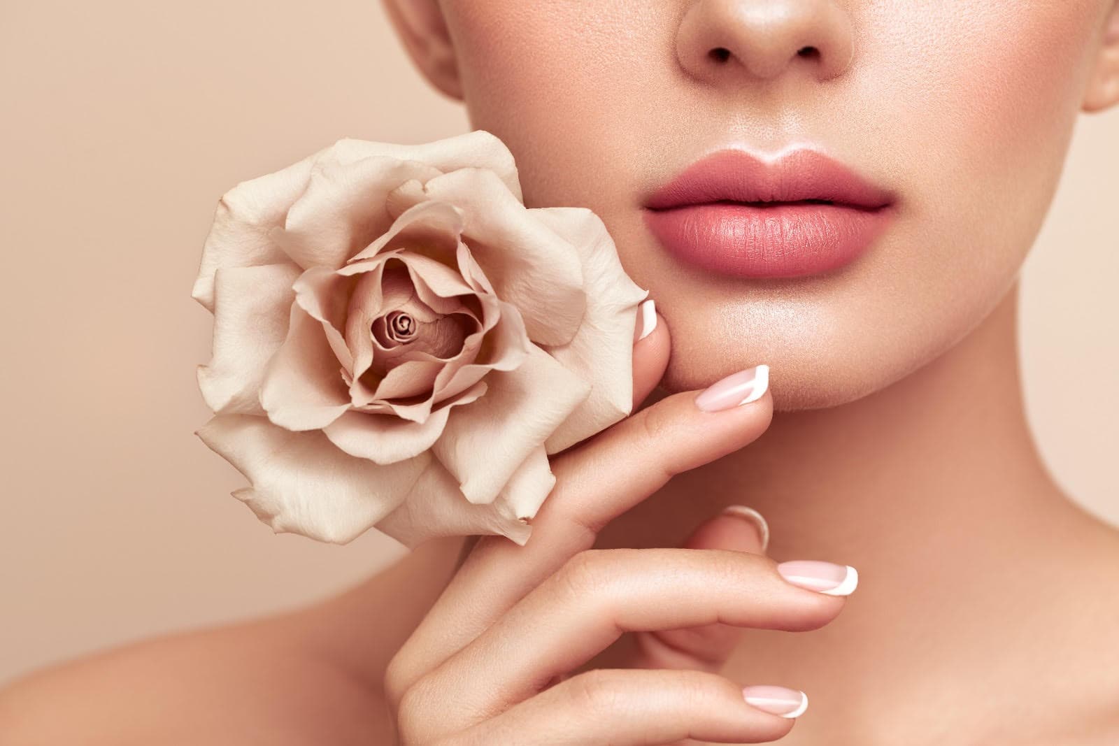 Close-up of a woman holding a cream rose to her face, with soft natural make-up and manicured nails